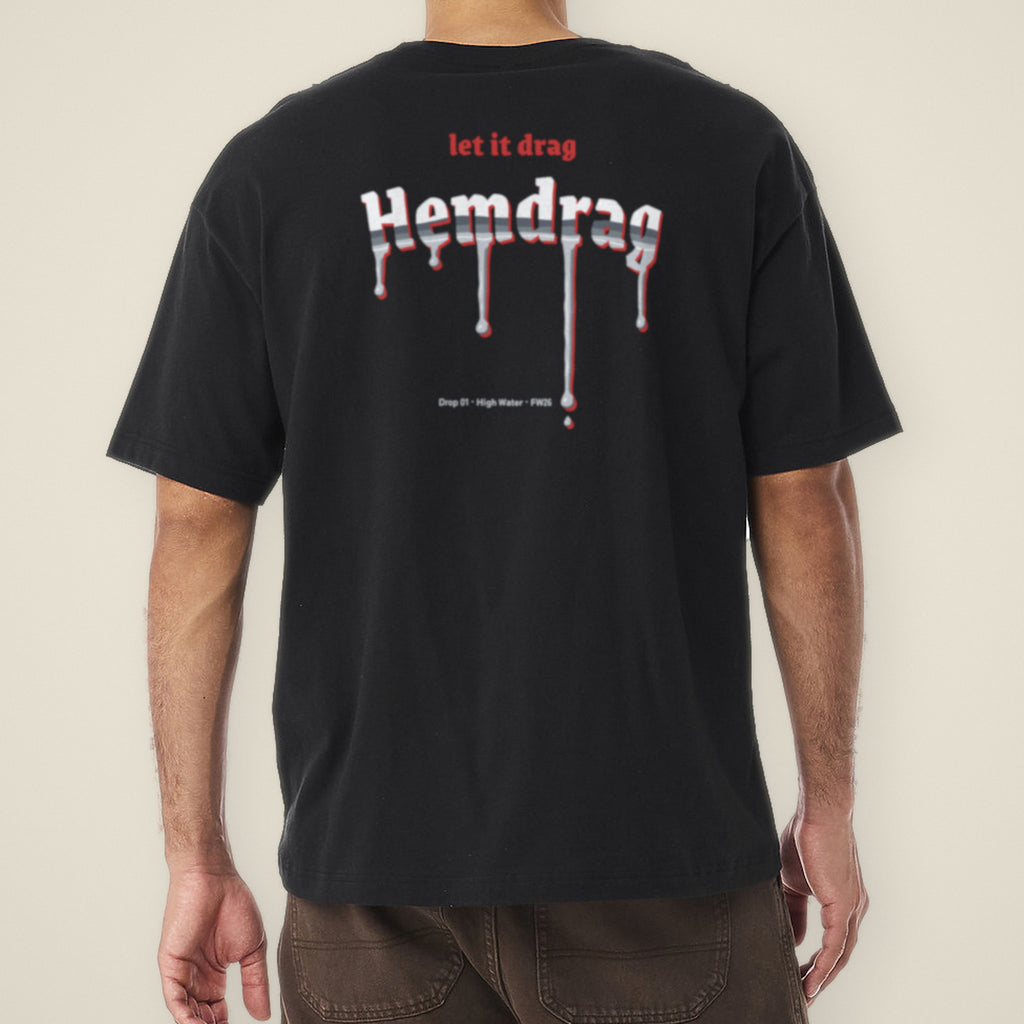 Digital preview: back view of a model wearing the black Let It Drag boxy tee. "let it drag" in red blackletter sits above the Hemdrag logo in chrome blackletter, with drips running off the letters and a small Drop 01 line beside the longest drip. The print was added digitally to a photo of the blank tee.