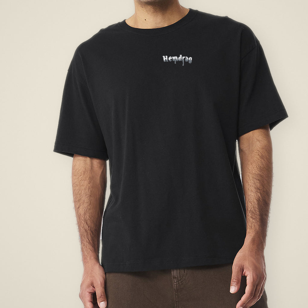 Digital preview: front of the black Let It Drag tee on a model, cropped at the chin, with a small chrome Hemdrag logo on the left chest. The logo was added digitally to a photo of the blank tee.