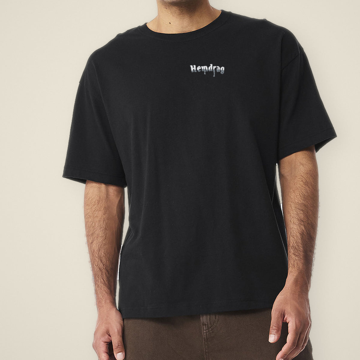 Digital preview: front of the black Let It Drag tee on a model, cropped at the chin, with a small chrome Hemdrag logo on the left chest. The logo was added digitally to a photo of the blank tee.