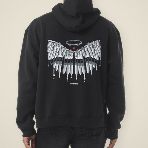 Digital preview: back of a model wearing the black No Wings Needed hoodie, hood down. Chrome barbed-wire wings drip down the back under a barbed-wire halo and a red drop, with a small Hemdrag in chrome blackletter below. Shown on a similar black hoodie used as a stand-in.