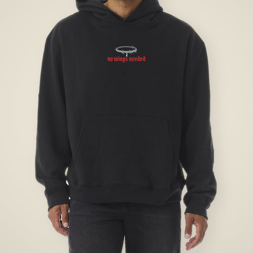 Digital preview: front of the black No Wings Needed hoodie on a model, cropped at the chin: a small chrome barbed-wire halo with one drip above "no wings needed" in red blackletter. Shown on a similar black hoodie used as a stand-in, from the same shoot as the back view.