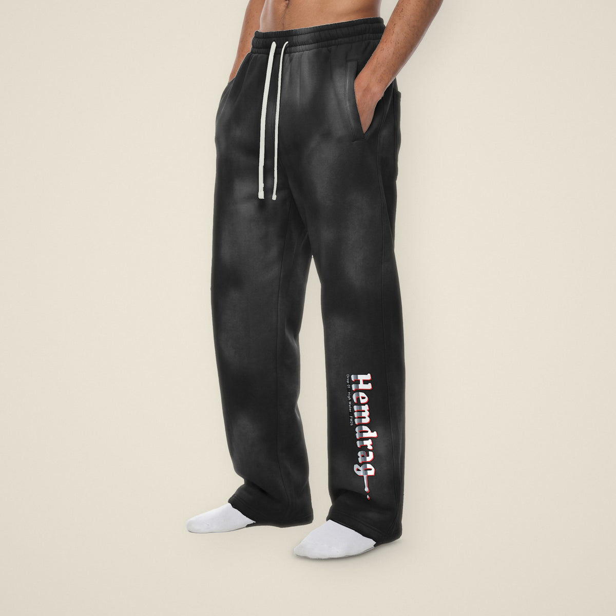 Digital preview: three-quarter view of a model in black sunfade Hemdrag wide-leg sweatpants. Hemdrag in chrome blackletter reads down the left lower leg and melts into one drip. The print and the black color were added digitally to a model photo.